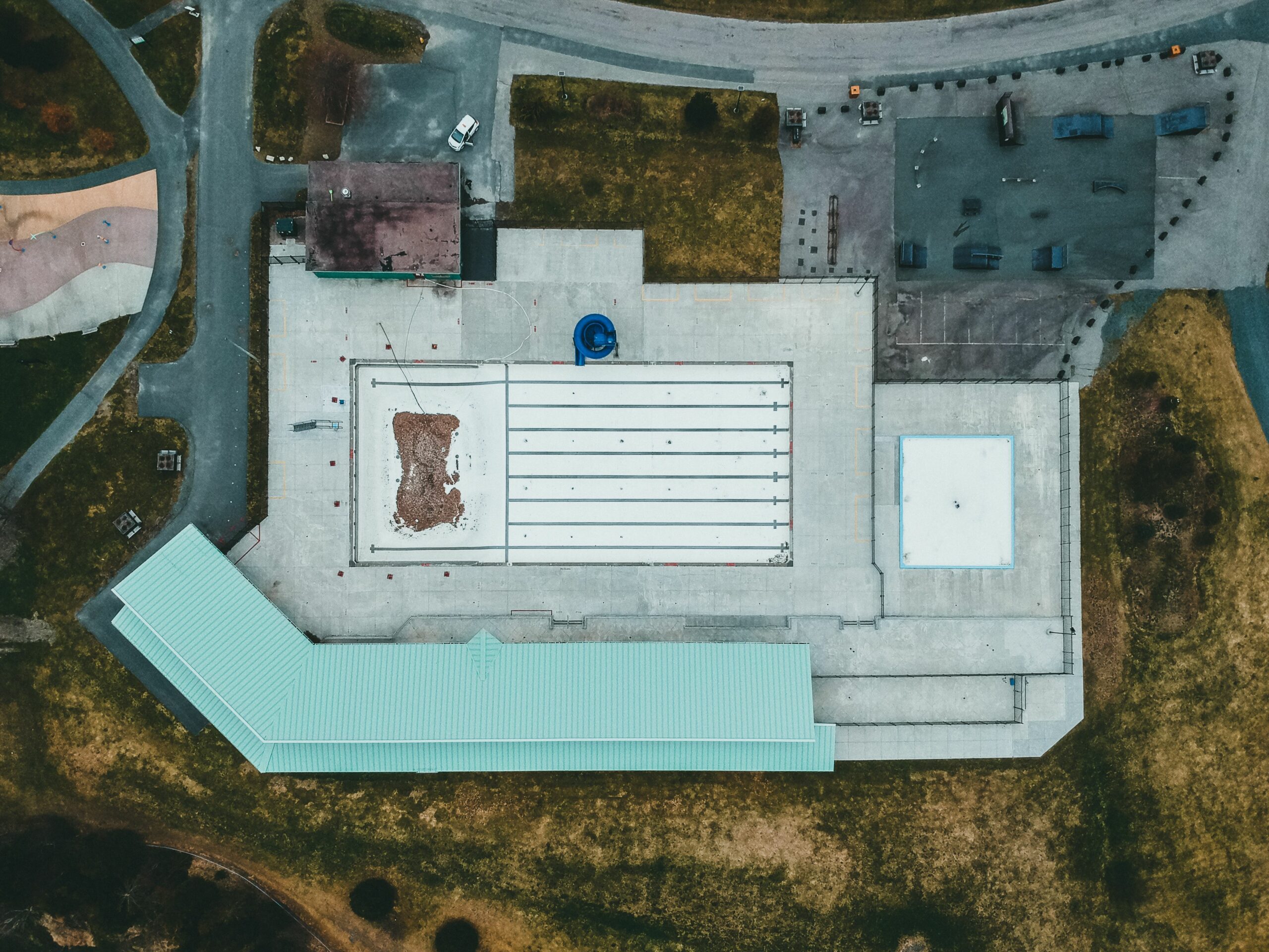 Aerial shot of a large building with a flat concrete rooftop and surrounding grassy area.